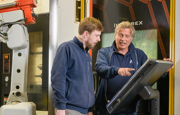 Werkgever die iets aanwijst op een digitaal paneel aan een medewerker in een werkplaats.